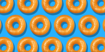 Creative pattern yellow donuts flat lay on pastel blue background. Minimal sweet food concept. Surreal original doughnuts cake top view for bakery. Abstract summer donut dessert.の写真素材