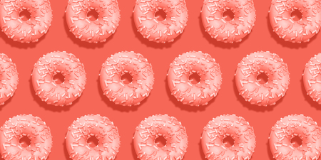 Creative pattern donuts flat lay on pastel coral background. Minimal sweet food concept. Surreal doughnuts cake top view for bakery. Abstract summer donut dessert. Living coral trend color 2019.の写真素材