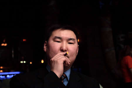The man smoking the cigar in the dark bar