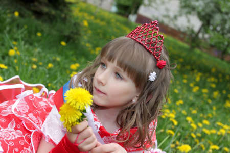 The girl in red dress with dandelions on lawn