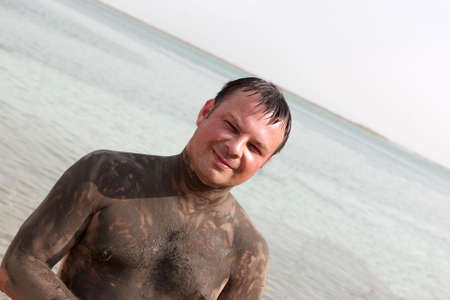 The man shows Mineral mud body on a beach of Dead seaの写真素材