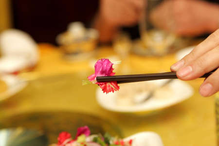 A woman holding red leaf by chopsticks in china restaurant, Beijingの写真素材