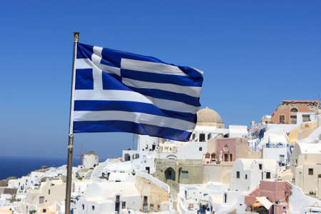 Greece flag on Oia background at Santorini island. It is town remains one of the foremost tourist attractions of the Aegean Sea. の写真素材