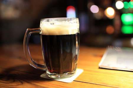 This is glass of dark beer on the wooden table in pub