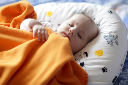 The baby boy sleeping under a orange blanket at homeのeditorial素材
