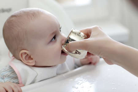 The baby boy drinking water from silver cup at homeの写真素材