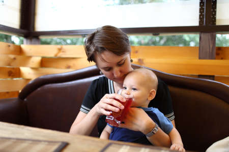 Mother gives to drink to her son in the restaurantの写真素材