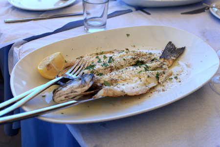 Cooked fish on a white plate in a seafood restaurantの写真素材