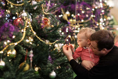 Baby is touching a bulb on a Christmas tree at homeの写真素材