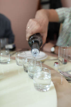 Man pours vodka from bottle into drinking glassesの写真素材