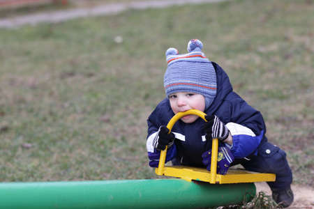 Toddler is holding handle of seesaw by teeth at autumnの写真素材