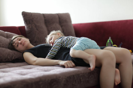 Toddler is sleeping on his mother at homeの写真素材