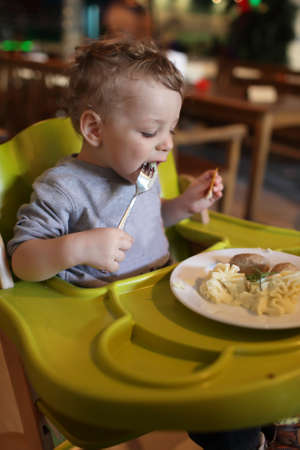 Toddler has a lunch in a high chair at a restaurantの写真素材
