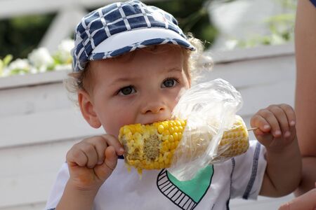 Toddler is eating boiled corn on the benchの写真素材