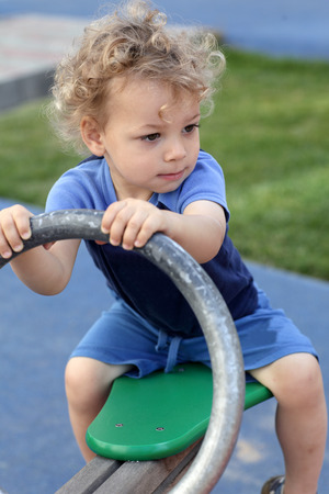 Curly child is playing at seesaw at playgroundの写真素材