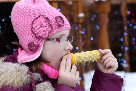 Kid is eating boiled corn in winterの写真素材