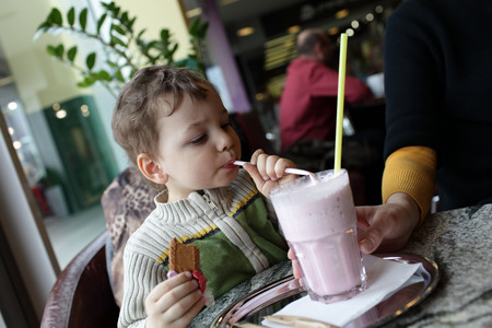 Child drinks milk strawberry smoothie in the cafeの写真素材