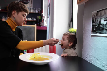 Son eats pumpkin soup from his motherの写真素材