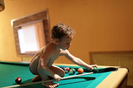Child sitting with billiard cue on the pool table