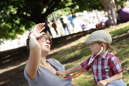 Child examines his mother using stethoscope outdoorの写真素材