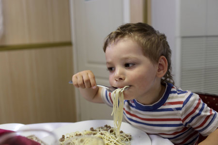 Child eating spaghetti with meat in the restaurantの写真素材