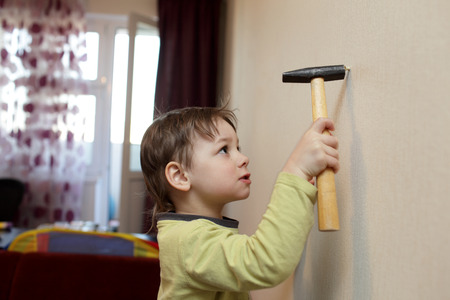 Boy hammering plastic anchor into wall at homeの写真素材