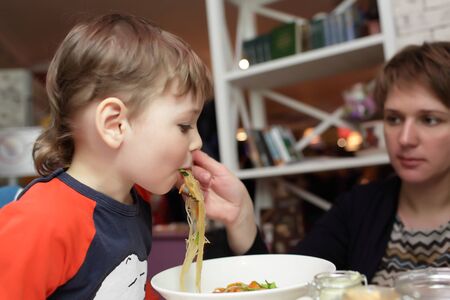Son eating noodles from her motherの写真素材
