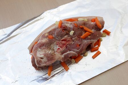 Raw pork shoulder with carrots on a foilの写真素材