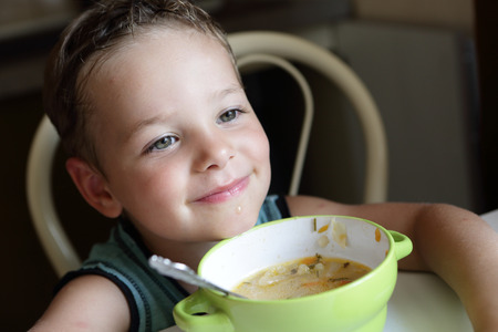 Smiling boy with plate of soup at homeの写真素材