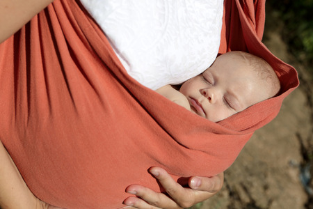 Newborn sleeping in the orange baby sling carrier outdoorの写真素材