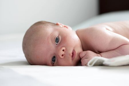 Thinking newborn baby lying on a bedの写真素材