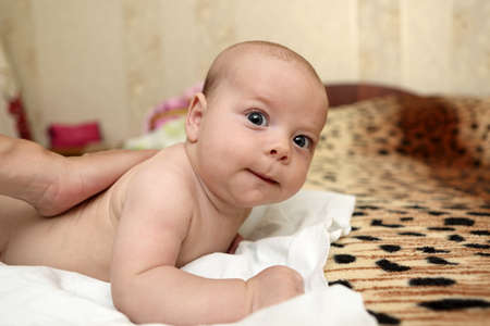 Mother massaging the baby's boy back on the bedの写真素材