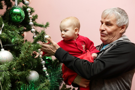 Grandfather with his grandson touching christmas tree on the wall backgroundの写真素材