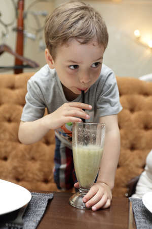 Boy is drinking smoothie in a cafeの写真素材