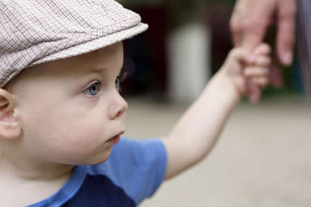Toddler in cap holding mother's hand in parkの写真素材