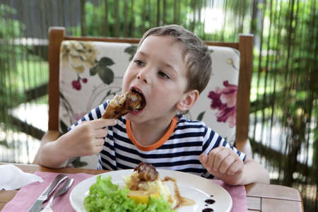 Child eating chicken leg in a cafeの写真素材