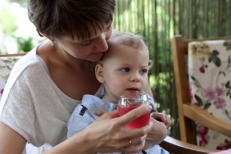 Toddler drinking juice from mother hands in cafeの写真素材