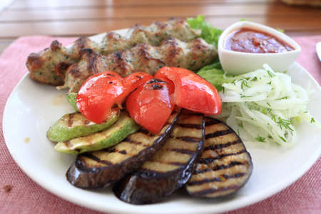 Plate with kebab and grilled vegetables on a table in restaurantの写真素材