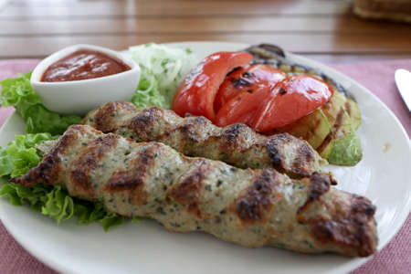 Plate with kebab and vegetables on a table in restaurantの写真素材