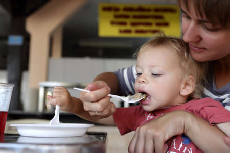 Mother feeding her son meatball in cafe