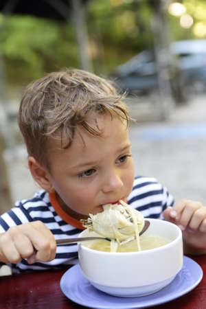 Boy eating chicken soup in a restaurantの写真素材