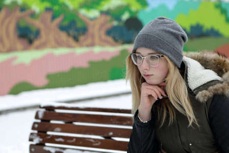 Portrait of a thinking teenager on bench in winter