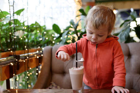 Toddler eating foam of cocoa in cafeの写真素材