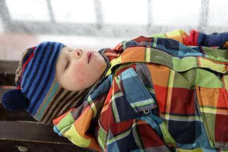 Boy sleeping on a bench in winterの写真素材