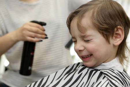Barber sprinkles water on child hair at barbershopの写真素材