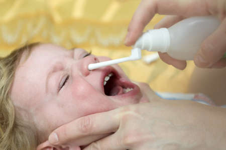 Boy Inhaling Nasal Spray on bed at homeの写真素材