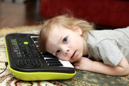 Kid lying and playing on synthesizer at homeの写真素材