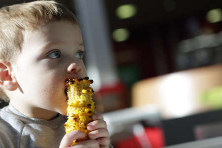 Kid biting grilled cob corn in cafeの写真素材