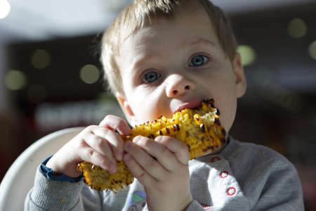 Boy biting grilled cob corn in cafeの写真素材