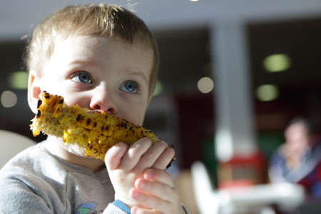Kid eating grilled cob corn in cafeの写真素材